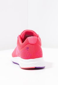 Vue arrière d'une chaussure de sport tricotée rose avec une finition texturée, présentant des accents violets sur la semelle et un logo de marque.