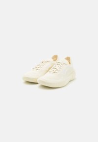 Jasne kremowe sneakersy z teksturowaną dzianiną na cholewce, z zaokrąglonym noskiem i amortyzowaną podeszwą. Zawierają sznurowanie i detal z logo.