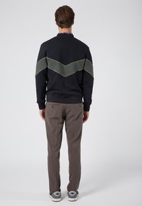 Felpa blu scuro con design a chevron verde oliva, cuciture beige. Abbinata a pantaloni a quadri marrone chiaro e sneaker grigie.