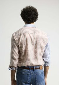 Camisa a rayas con rayas verticales rosas y blancas por un lado, y rayas azules y blancas por el otro. Cuenta con un cuello y mangas remangadas.