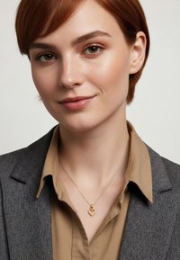 Goldenes Herzanhänger-Halskette an einer zarten Kette, getragen über einem beigen Hemd mit Kragen und einem grauen Fischgrät-Blazer. Dezenter Glanz und filigranes Design.