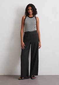 Pantalons larges noirs associés à un haut sans manches rayé noir et blanc. Le tissu semble doux, avec une texture lisse et une taille élastique.