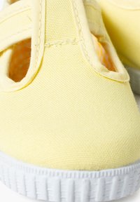 Scarpe da ginnastica gialle in tela con superficie testurizzata, caratterizzate da una forma arrotondata, una fascia elastica per la vestibilità e una suola in gomma bianca.