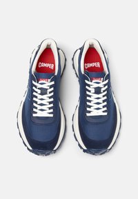 Sneaker blu navy con lacci bianchi, solette rosse e suole in gomma spesse. La tomaia in tessuto presenta accenti sintetici e dettagli testurizzati.