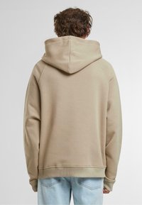 Beige kapucnis pulóver, húzózsinórral, raglán ujjal és bordás mandzsettával. Puha tapintású és laza fazonú, világoskék farmerrel párosítva.