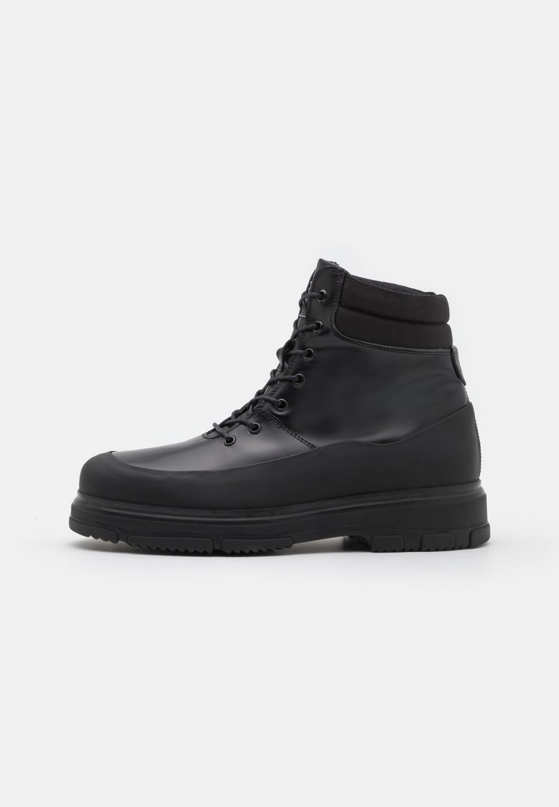Botte noire montante à lacets avec col rembourré à la cheville et semelle épaisse en caoutchouc, présentée de profil sur fond blanc.