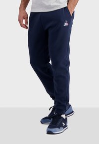 Marineblauwe joggingsbroek van een zachte stof met een elastische tailleband, voorzien van zijzakken en een klein logo op de bovenbeen.