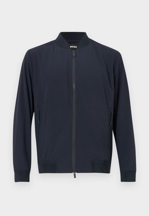 Marinblå bomberjacka med dragkedja fram, ribbad krage och manschetter, samt två sidofickor med dolda dragkedjor. Slät, lättviktig tyg.