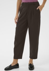 Brown high-waisted trousers with a loose fit, featuring front pleats and side pockets, paired with black loafers for a polished look.