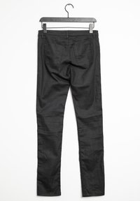 Pantalones de mezclilla negros con un ajuste ceñido. Cuentan con dos bolsillos traseros y una superficie de textura suave. Cuelgan de una percha de plástico negra.