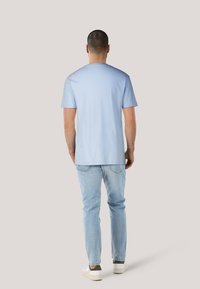 Camiseta de algodón azul claro con mangas cortas, diseño de cuello redondo y corte recto, combinada con jeans azul claro y zapatillas blancas.