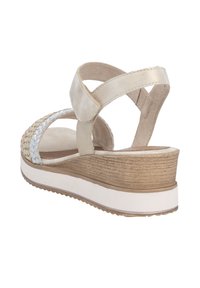 Wedge sandals with a braided metallic strap, beige upper material, tan wooden-effect wedge, and a white rubber sole. Crossed ankle strap design.