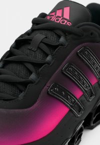 Čierna atletická obuv s prechodom ružovej farby, textúrovanou sieťovinou na vrchu, výraznými čiernymi šnúrkami a ikonickým logom s tromi pásikmi na boku.