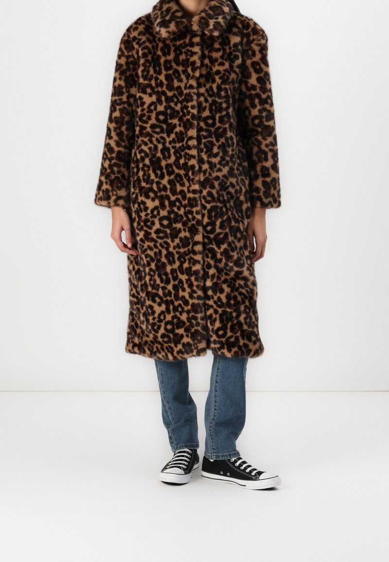 Jas van faux fur met luipaardprint, voorzien van een reverskraag, lange mouwen en een midilange snit, gecombineerd met blauw denim en zwarte sneakers.
