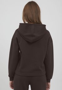 Bruine katoenen hoodie met een grote, gevoerde capuchon. Beschikt over verlaagde schoudernaden en ribgebreide manchetten. Glad oppervlak, eenvoudig ontwerp, geen zichtbare patronen.