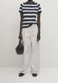 Navy and white striped knit top with short sleeves, paired with cream wide-leg trousers. Black woven handbag and dark sandals complete the look.