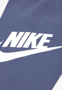Teren de țesătură de marcă Nike, de culoare albastră închisă, cu o suprafață texturată. Logo-ul mare de culoare albă prezintă litere îndrăznețe și un design de swoosh.