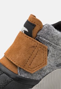 Bruna mockaskinnsneakers med grått filt, utrustade med ett kardborreband, svart gummisula och texturerade detaljer på ovandelen.