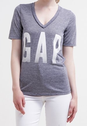 Szary, melanżowy t-shirt z krótkim rękawem i dekoltem w serek, z dużymi białymi literami "GAP" na przodzie. Lekka, casualowa tkanina.