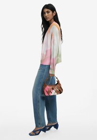 Pastel-colored, long-sleeve sweater with a gradient pattern, light denim jeans, and a multicolored woven handbag; blue strappy heels.