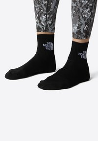 Sorte crew-sokker laget av mykt strikket materiale, med en hvit logo. Kombinert med mønstrede grå tights.