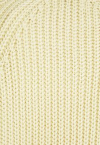 Gros plan sur un tissu tricoté couleur crème avec un motif de point vertical côtelé et des fibres de fil texturées.