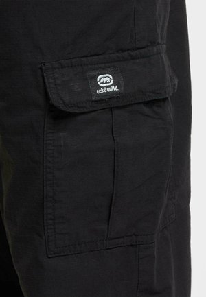 Black cargo shorts with a textured fabric. Features a large side pocket with a flap, and a visible logo tag.