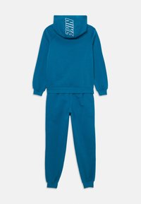 Tirkīzs Nike džemperis ar lielu logo mugurā un atbilstošām sporta biksēm. Gluda, mīksta auduma, ar elastīgām aprocēm pie piedurknēm un potītēm.
