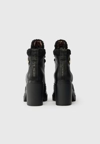 Svarta läderstövletter med klack, en fluffig krage och texturerad bakpanel. Har en blockklack och metallaccenter.