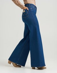 Jeans a gamba larga blu con vita alta e cuciture a contrasto. Presentano una tasca posteriore con etichetta e fondo svasato. Abbinati a scarpe metalliche.