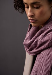 Herringbone-patterned scarf in muted purple hues, soft texture, draped closely around the neck, complementing a neutral top.