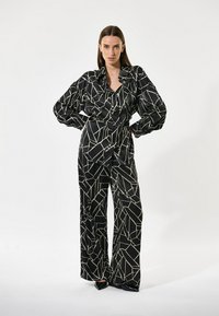 Sort mønstret jakkesæt lavet af glat stof, prydet med et geometrisk crememønster, med brede ben og voluminøse ærmer.