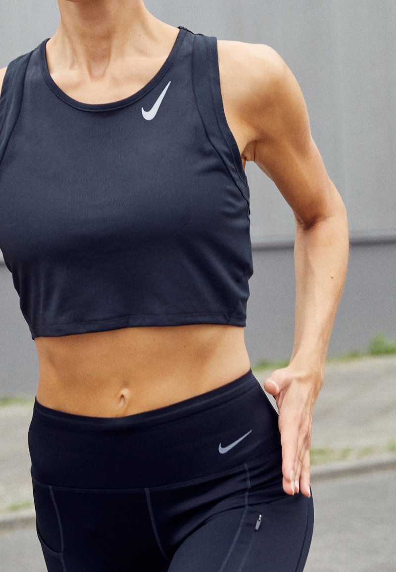 Top sportivo nero croppato con scollatura rotonda e logo Nike; abbinato a leggings neri a vita alta con una piccola tasca.