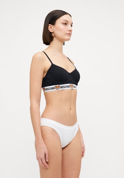 Crni bralet s podesivim trakama i bendom s logom medvjeda Moschino; u kombinaciji s bijelim gaćicama. Glatka tkanina, jednostavan dizajn i uski stil.