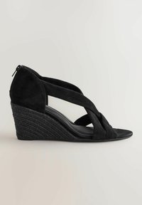 Sandales à talon en cuir suédé noir, avec des sangles croisées, une fermeture éclair à l'arrière et un talon en jute texturé.