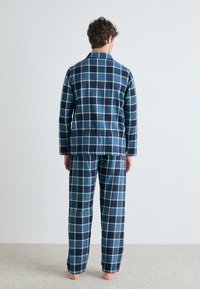 Ensemble de pyjama en flanelle à carreaux bleus et navy, comprenant une veste à col et un pantalon assorti, avec une coupe décontractée et une texture douce.