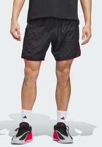 Μαύρα αθλητικά σορτς με κυματιστό μοτίβο, διακοσμημένα με κόκκινες ρίγες. Φοριούνται με λευκές κάλτσες και μαύρα-κόκκινα αθλητικά παπούτσια.