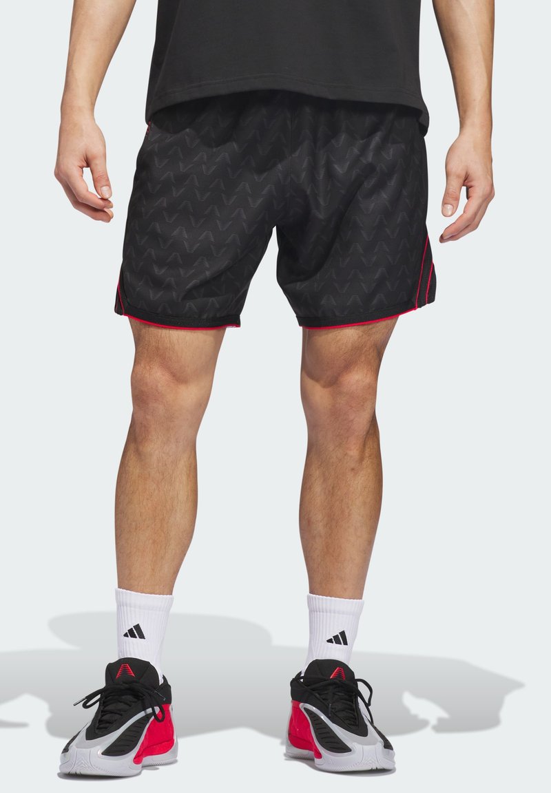 Μαύρα αθλητικά σορτς με κυματιστό μοτίβο, διακοσμημένα με κόκκινες ρίγες. Φοριούνται με λευκές κάλτσες και μαύρα-κόκκινα αθλητικά παπούτσια.