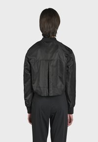 Čierna skrátená bomber bunda s hladkým, lesklým povrchom, rebrovaným golierom a manžetami, a detailom na zadnej strane. Jednoduchý a elegantný dizajn.