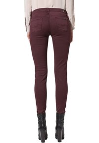 Jeans skinny burdeos con una textura suave, que cuentan con dos bolsillos traseros y una cinturilla de altura media. Combinados con botas negras de tacón alto.