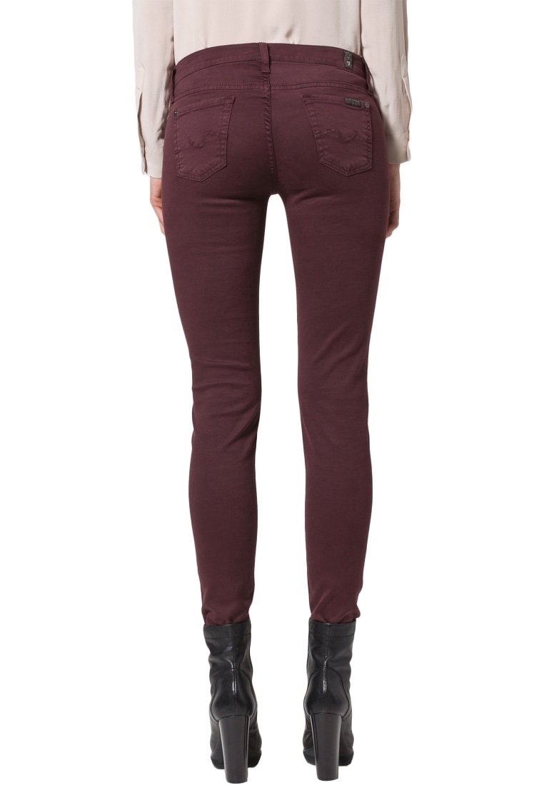 Jeans skinny burdeos con una textura suave, que cuentan con dos bolsillos traseros y una cinturilla de altura media. Combinados con botas negras de tacón alto.