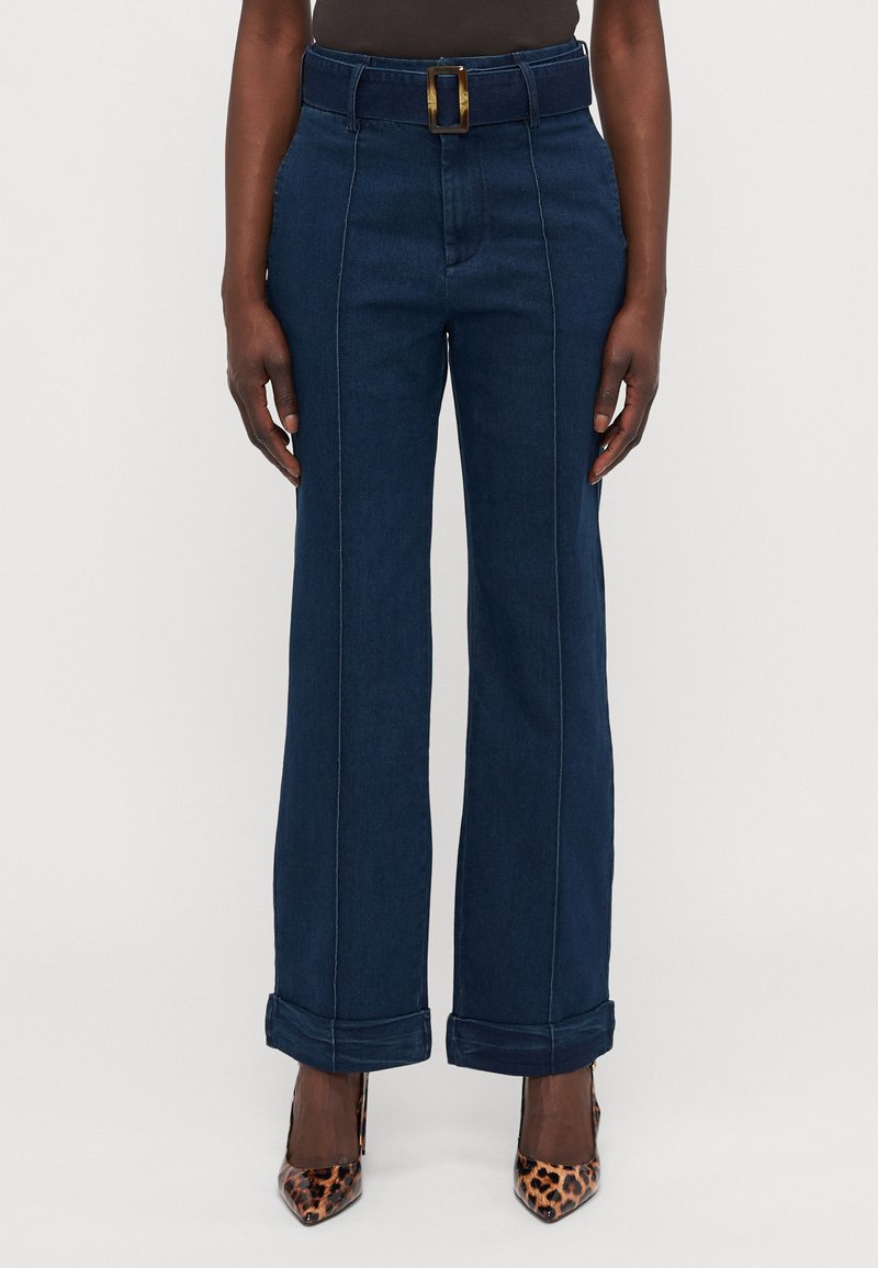 Høyt midjede, vide ben i mørk denim med belte som har en messingspenne, rullede mansjetter og kontrasterende hvite sømmer.