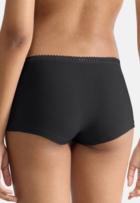 Sort boyshort undertøj med en bølget blondekant, glat stoffinish og en tæt pasform, der viser bagsiden og en del af lårene.