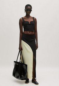 Zwarte cropped top met een V-hals, gecombineerd met een zwart en lichtgeel asymmetrische rok met een zijscheur. Model draagt een zwarte totebag.