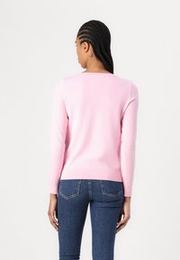 Lys rosa strikket genser med rund hals, lange ermer og ribbestrikkede mansjetter, parret med blå denim jeans. Glatt tekstur, tettsittende design.