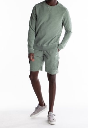 Sweatshirt en coton vert avec un col rond et des poignets côtelés, associé à un short cargo assorti avec des poches et un ourlet distendu.