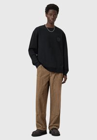 Sudadera negra con cuello redondo y logotipo bordado, combinada con pantalones de pana marrones y zapatos negros. Diseño simple y casual.