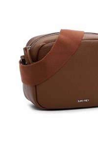 Borsa a tracolla in pelle marrone con finitura testurizzata, dotata di una larga tracolla in tessuto e chiusura con zip, con il nome del marchio impresso sul lato.