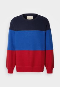 Sudadera con cuello redondo que presenta bloques de color horizontales en azul marino, azul y rojo. Fabricada con una tela suave y con puños y dobladillo acanalados.