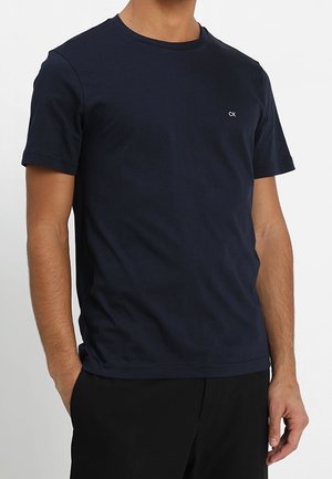 T-shirt col rond marine en coton lisse, avec un petit logo CK blanc sur la poitrine, des manches courtes et une coupe décontractée.